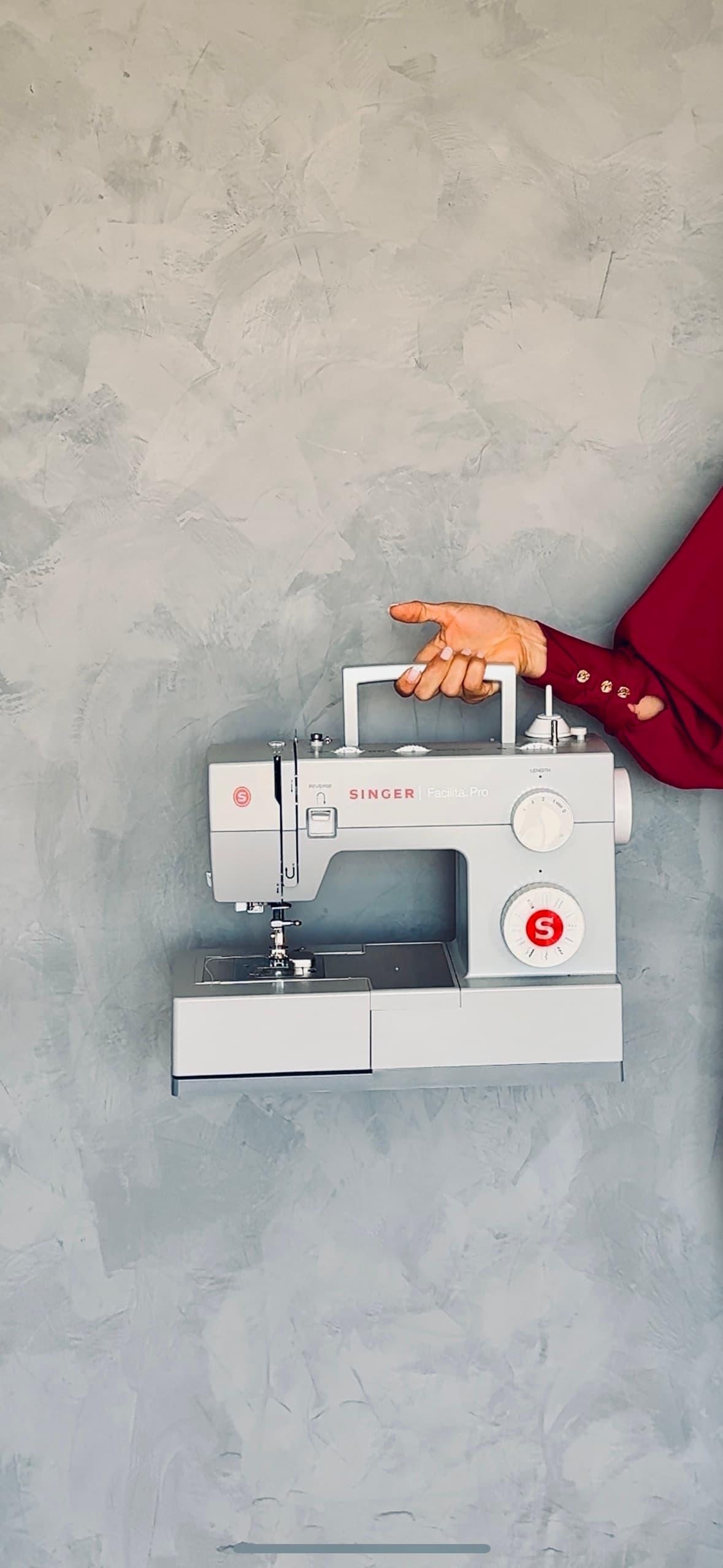 Mão apontando para máquina de costura Singer